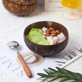 Coconut wood dessert bowl filled with matcha ice cream, almonds, and coconut flakes, styled with wooden spoon on white surfac