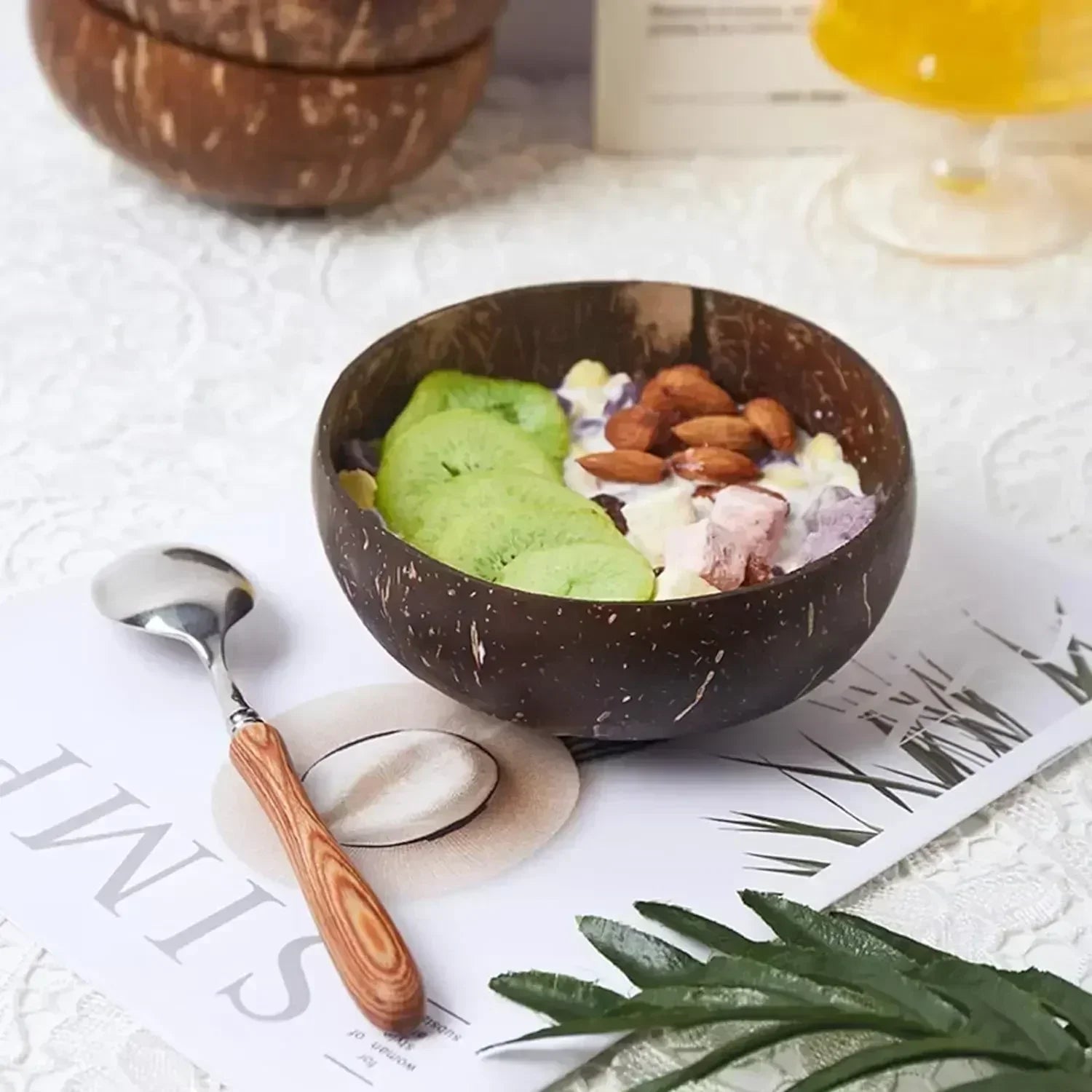 Coconut wood dessert bowl filled with matcha ice cream, almonds, and coconut flakes, styled with wooden spoon on white surfac