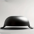 Black cast iron double-handle pot with curved dome lid, viewed from side profile against white background, showing sturdy coo