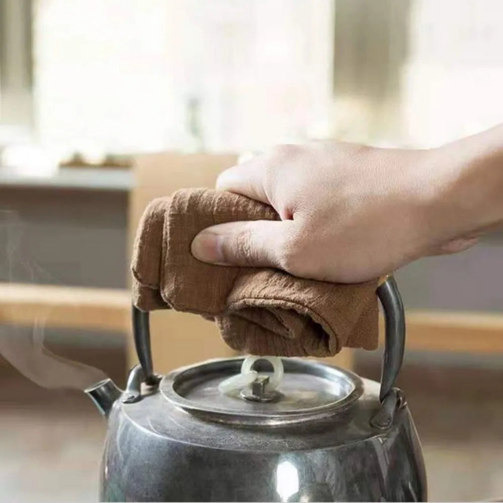 Organic cotton cleaning cloth being used to safely hold hot kettle handle, demonstrating absorbent towel functionality in kit