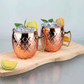 Two copper hammered finish mugs with ice, lime and orange slices on wooden board, mint garnish visible.