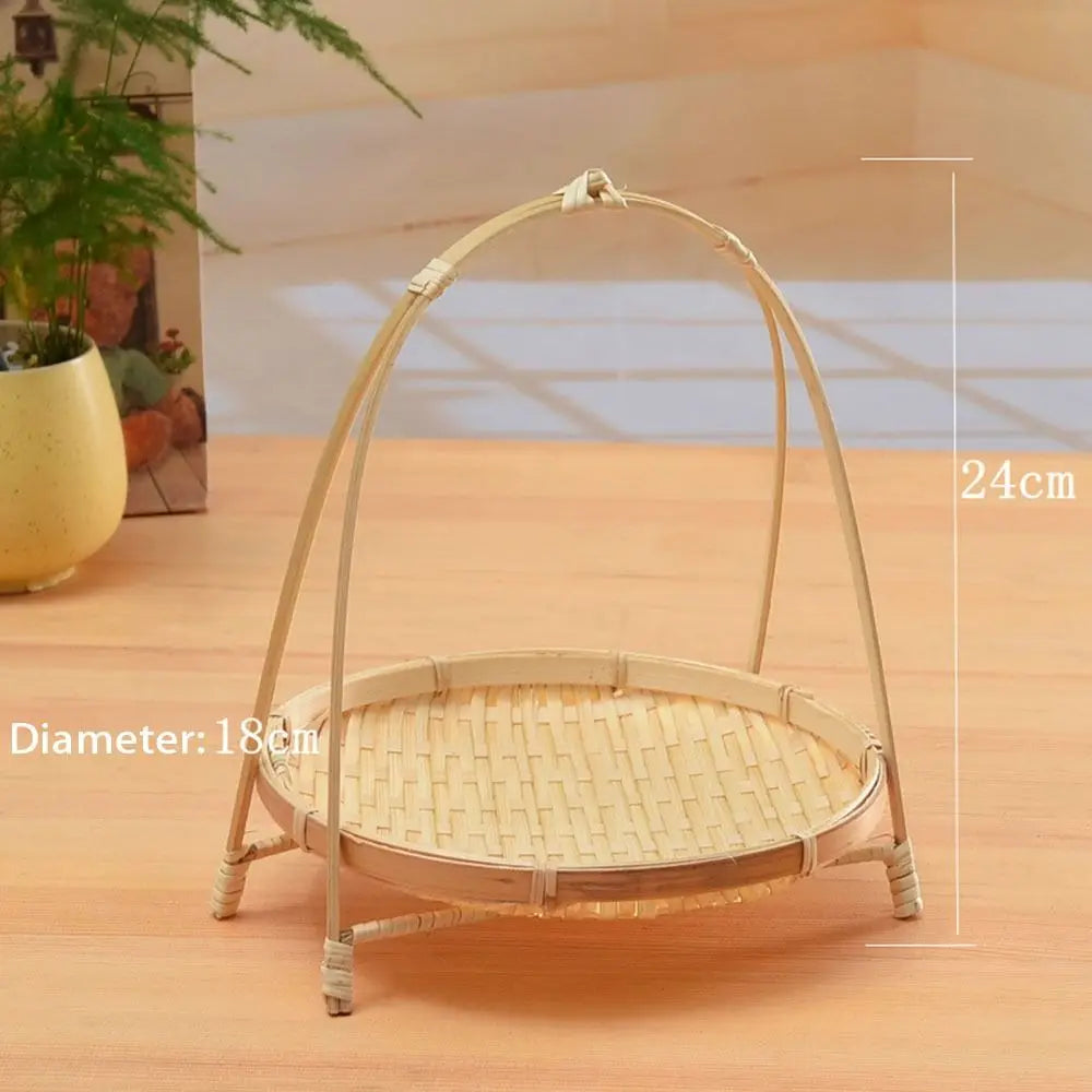Woven bamboo basket with arched handles, 18cm diameter and 24cm height, displayed on wooden surface with potted plants.