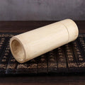 Natural bamboo cylindrical tea storage canister with hollow interior, displayed on decorative black box with gold Chinese cha