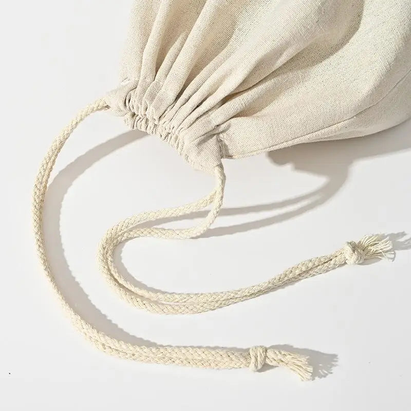 Handmade organic linen bread bag with drawstring closure, displayed flat showing natural cream fabric and braided cord ties.