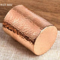 Handcrafted pure copper mug with hammered texture detail and smooth flat base, displayed on neutral fabric.