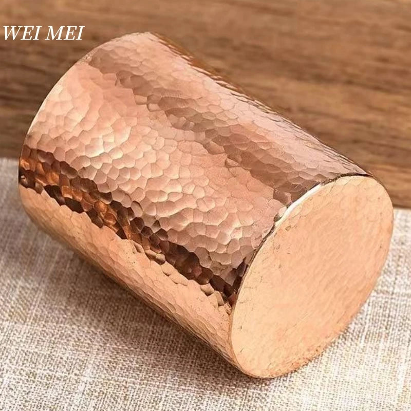 Handcrafted pure copper mug with hammered texture detail and smooth flat base, displayed on neutral fabric.