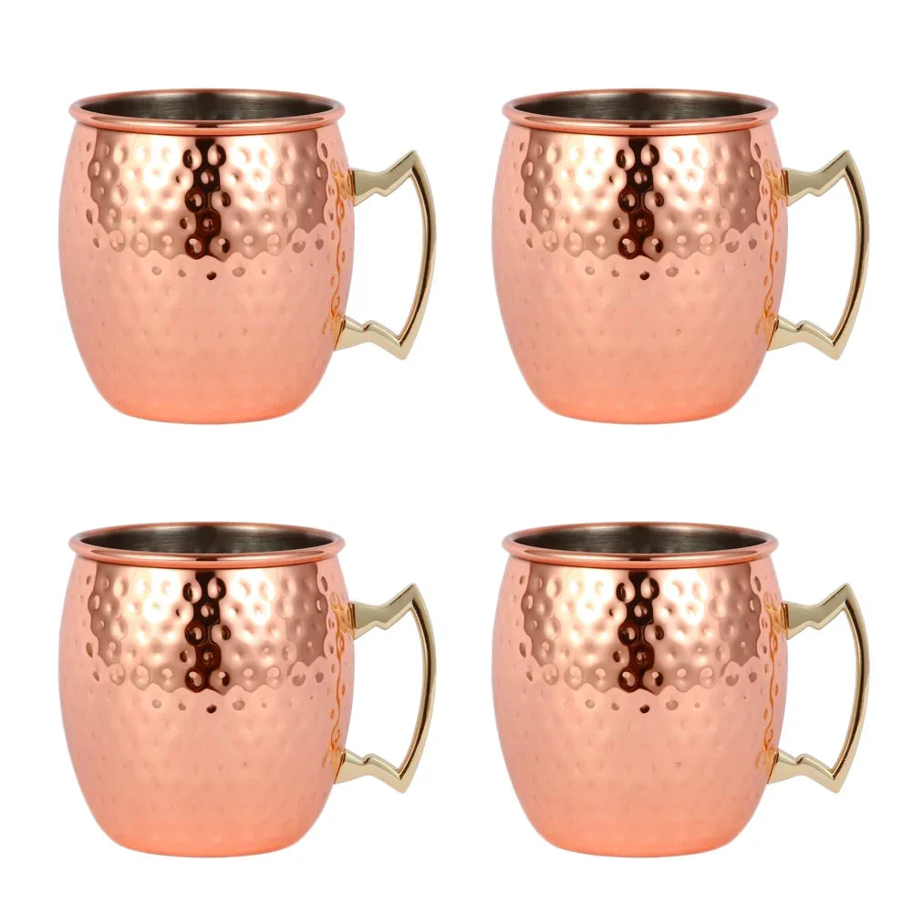 Set of four copper Moscow mule mugs with hammered finish, stainless steel interiors, and brass handles on white background.