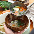 Handcrafted wooden serving bowl holding vegetable soup with ladle, displaying natural coconut shell material and eco-friendly