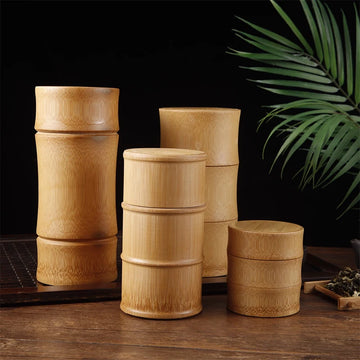 Set of four natural bamboo storage containers with lids in varying heights, displayed on wooden surface with green plant and 