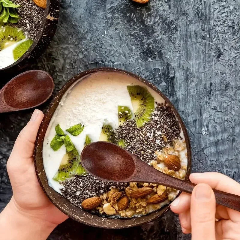 Handcrafted wooden serving bowl filled with yogurt, chia seeds, kiwi slices, and nuts, held in hands with wooden spoon.
