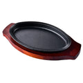 Cast iron oval griddle pan with decorative rope rim on dark wood serving board base