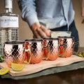 Hammered copper insulated travel mugs with brass handles arranged on wooden board beside The Botanist gin bottle and lime gar
