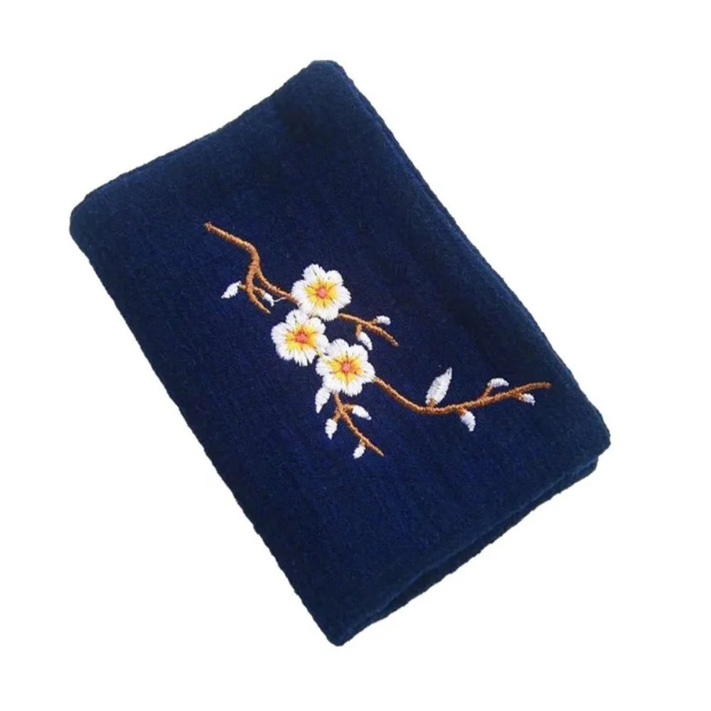 Organic cotton embroidered cleaning cloths in brown and green with white floral designs, displayed with wooden combs on gray 