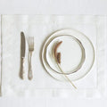 Elegant place setting with stacked cream plates, ornamental fork and knife on natural linen placemat, dried pampas grass garn