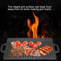 Cast iron dual-sided griddle with ridged surface grilling meat, tomatoes, and sausages over flames, showcasing grill marks.