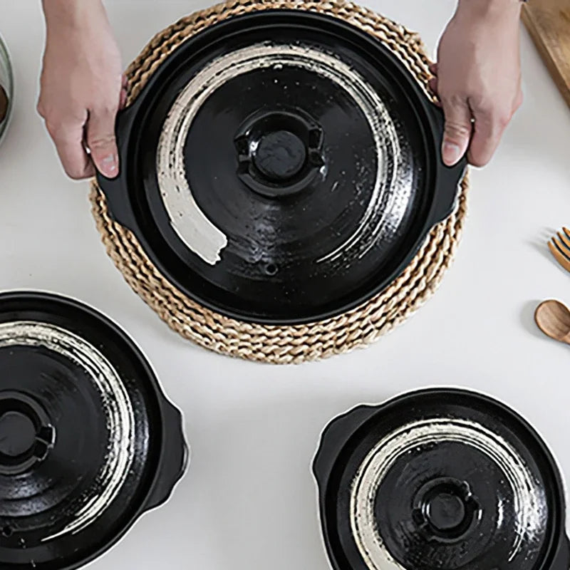 Black earthenware casserole pot with natural woven seagrass handle, lid shown, rustic artisanal design for slow cooking.