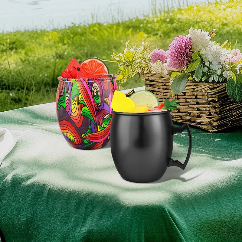 Black insulated copper travel mug with handle, filled with yellow beverage and lime slice, displayed on green tablecloth outd
