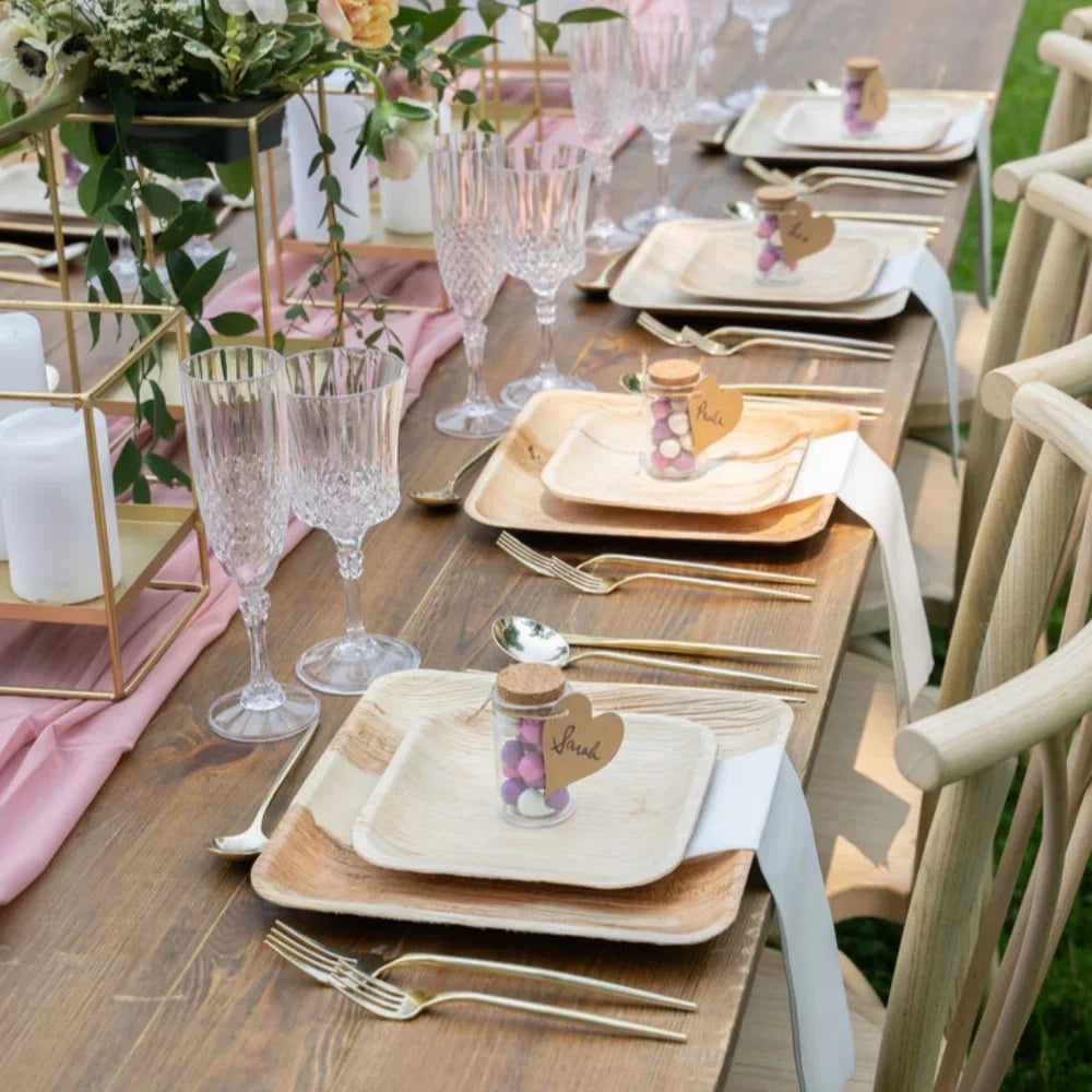 Eco-friendly palm leaf plates in natural wood tones displayed on an elegant table setting with gold cutlery, crystal glasses,