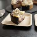 Eco-friendly palm leaf plate holding a slice of chocolate cake with whipped cream topping, demonstrating biodegradable dinner