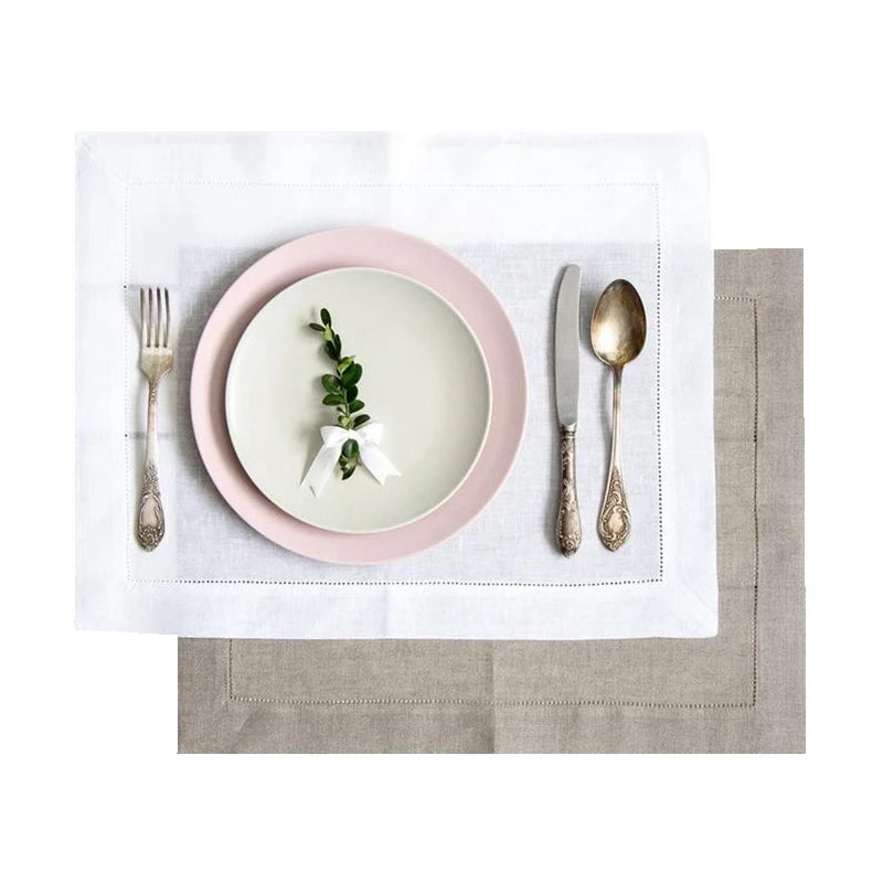 Elegant place setting with natural linen napkin, pink plate, and vintage silverware on white hempstitched linen placemat