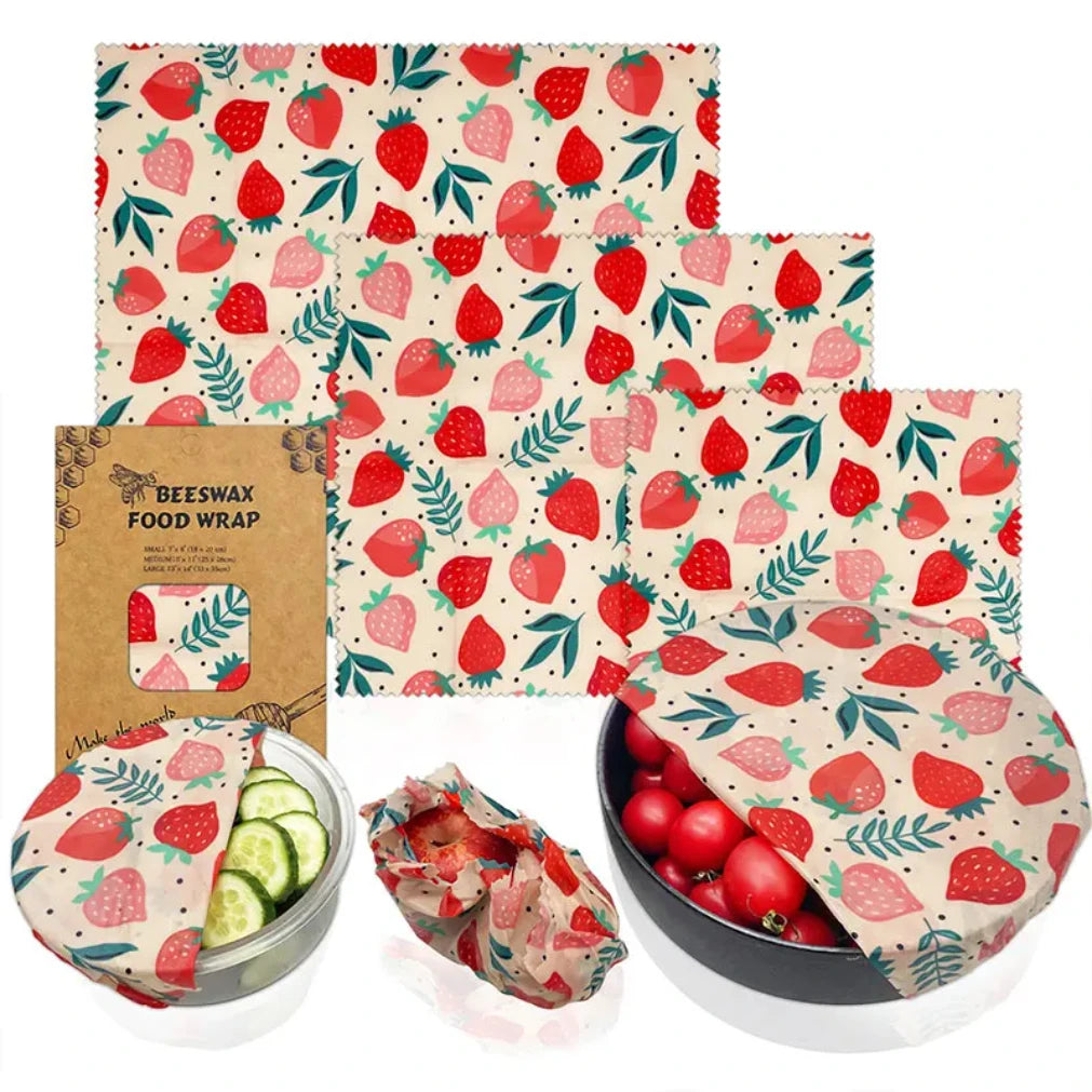 Beeswax food wrap set with strawberry pattern, showing three reusable wraps covering bowl, produce, and tomatoes on cream bac