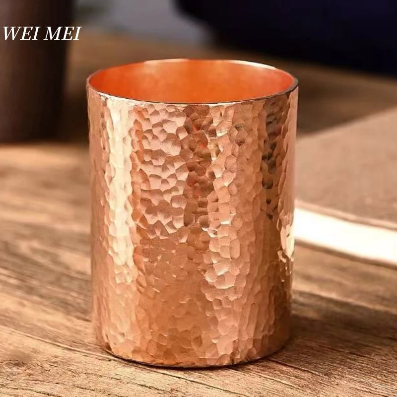 Handcrafted pure copper mug with hammered texture and orange enamel interior, displayed on wooden surface.