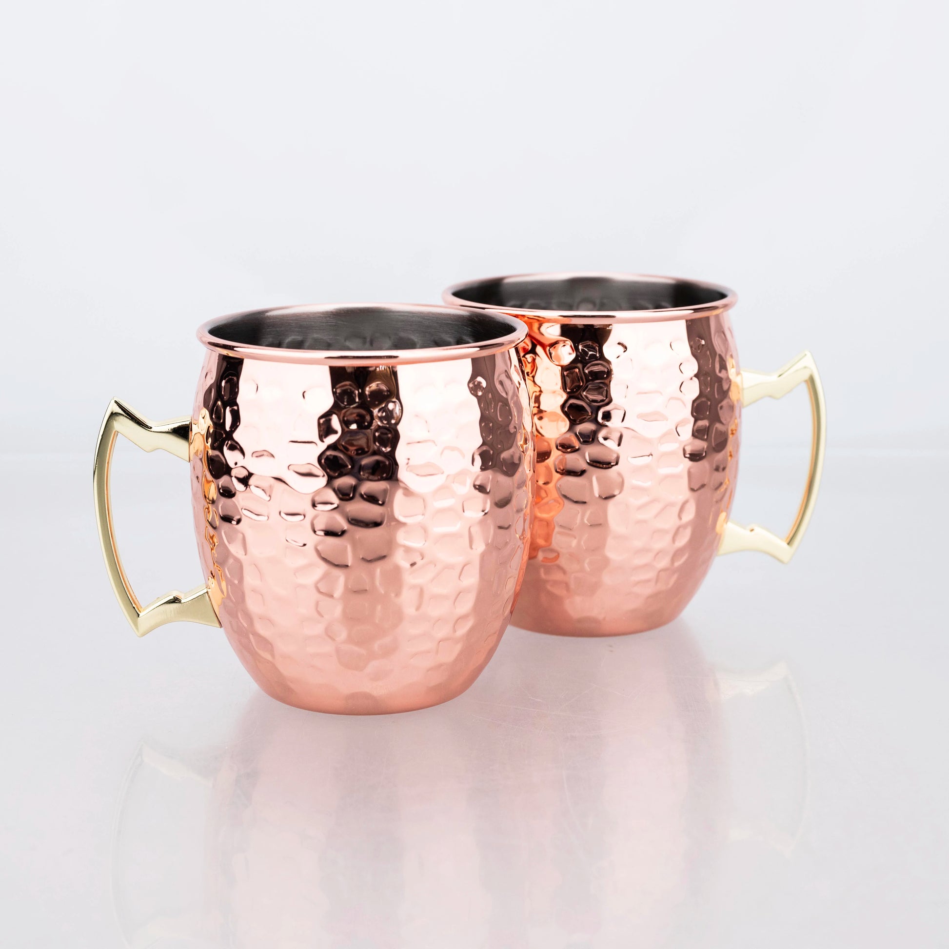 Two hammered copper travel cups with brass handles and dark interior lining on white background.