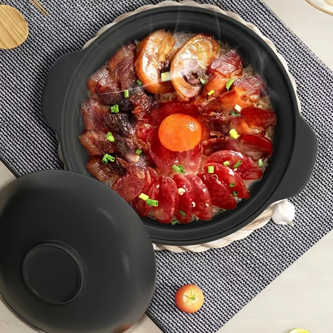 Black ceramic clay cooking pot with lid, filled with raw beef slices, mushrooms, carrot, and green onions on textile surface.