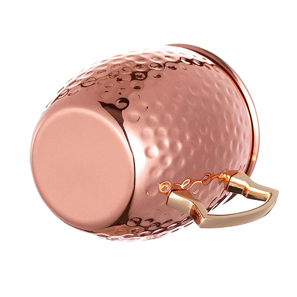 Rose gold hammered Moscow mule mug with smooth circular front panel and rose gold handle against white background.
