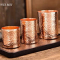 Three handcrafted copper glasses with hammered texture on wooden tray, showcasing vintage artisanal tableware in graduating s