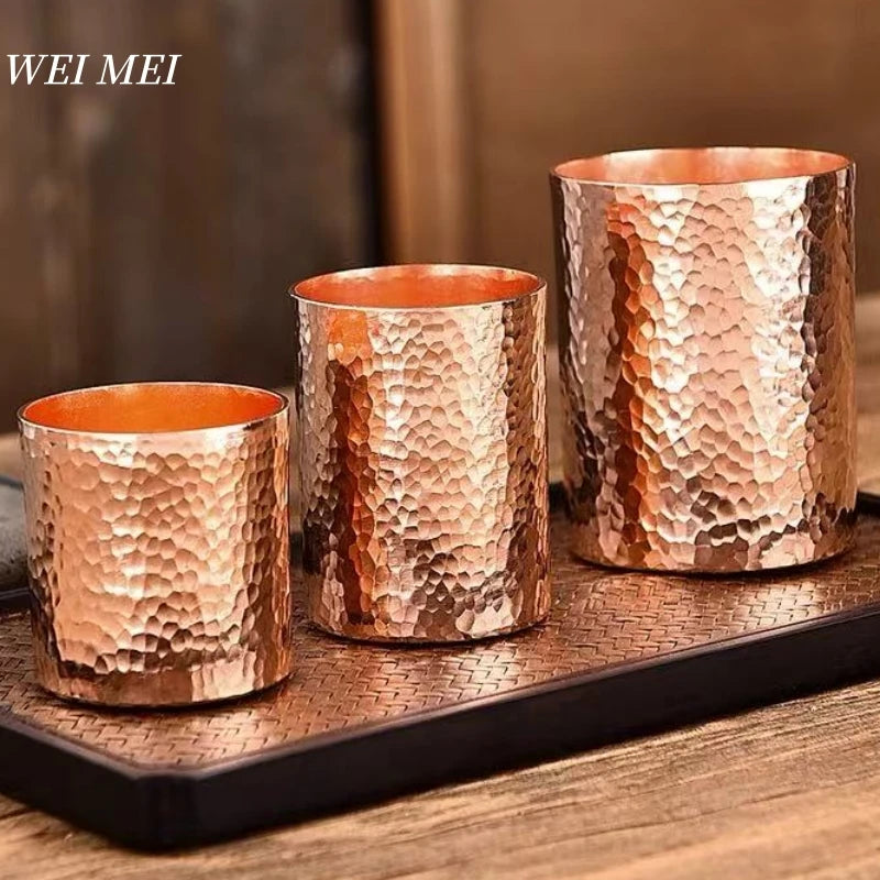 Three handcrafted copper glasses with hammered texture on wooden tray, showcasing vintage artisanal tableware in graduating s