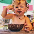 Handcrafted natural wooden serving salad bowl with rustic finish, displayed with child using wooden spoon.