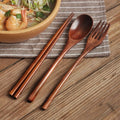 Wooden cutlery set with chopsticks, spoon, and fork on striped linen napkin beside Asian noodle bowl on wooden table.