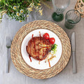 Handwoven rattan round placemat with white ceramic plate displaying creative food art, flanked by fork and knife on neutral l