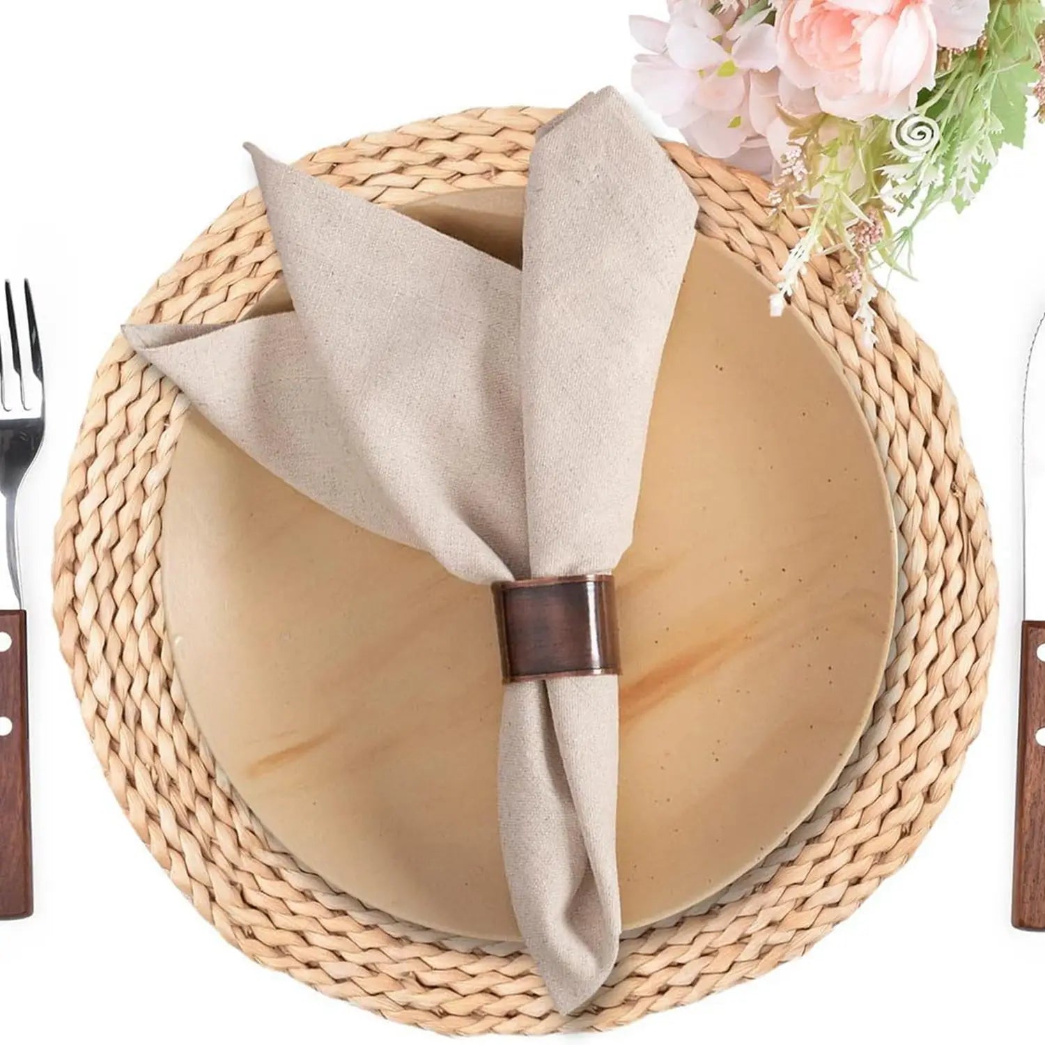 Beige cotton linen napkin with brown napkin ring on round woven placemat, styled with dinnerware and pink flowers
