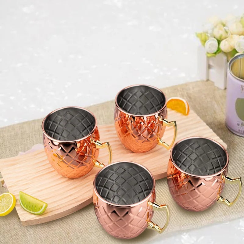 Four hammered copper Moscow Mule mugs with black interior linings and brass handles on a wooden board with lime slices.