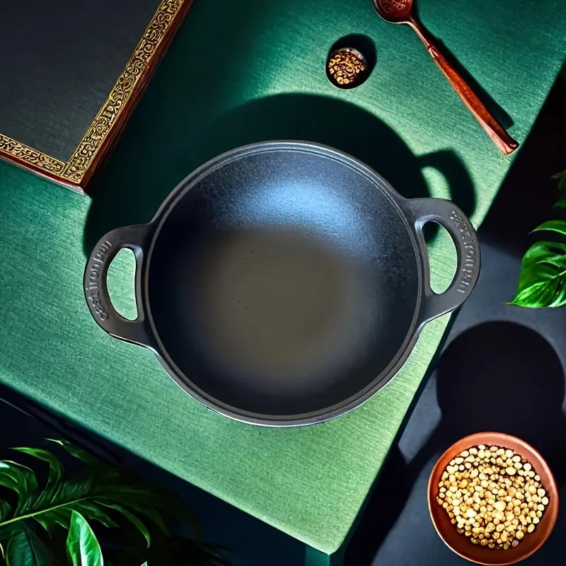 Cast iron double-handle ingot pot with seasoned black finish, displayed on green fabric with decorative items and ingredients
