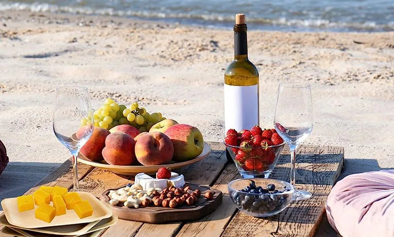 Biodegradable palm leaf plates displaying fresh fruits and wine at a beach picnic setup, showcasing eco-friendly dinnerware.