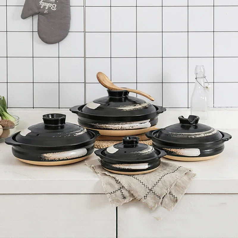 Blue and white ceramic casserole pots with leaf designs, displayed on wooden surface with woven placemats and potted plants.