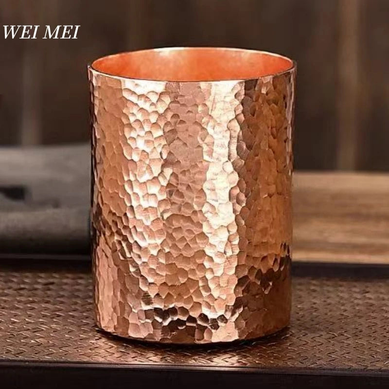 Handcrafted copper mugs with hammered texture in three sizes, filled with mint beverage, displayed on wooden surface with her