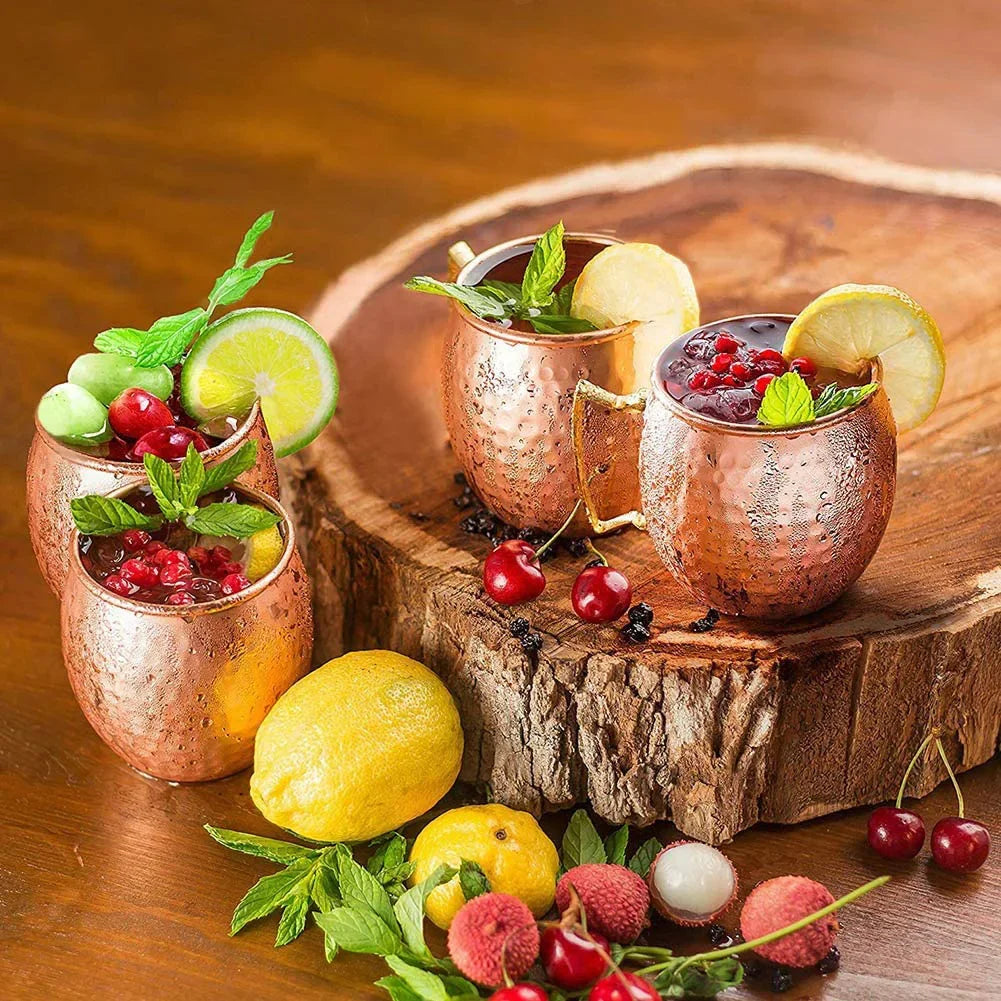 Three copper Moscow mule mugs filled with berries and citrus, garnished with fresh mint and lime slices, displayed on wooden 