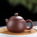 Purple clay teapot on wooden trivet, 200ml handmade traditional tea pot with lid and handle, displayed against blurred green 
