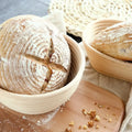 Natural rattan bread proofing basket with artisan sourdough loaves showing scored crust and flour dusting on wooden surface.