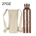 Copper water bottle with hammered design next to cream canvas carry bag with shoulder straps, 27oz capacity
