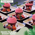 Square palm leaf dessert plates with chocolate cupcakes topped with pink frosting, fresh berries, and edible flowers.