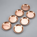 Seven handcrafted pure copper dining plates arranged on dark background, varying sizes, polished red copper finish with raise