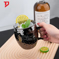 Black hammered copper insulated travel mug filled with ice, lemon slice, and mint leaf, held in hand on wooden surface