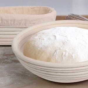 Natural rattan bread proofing basket with oval shape, featuring dusted flour and proofing dough inside, handmade banneton des