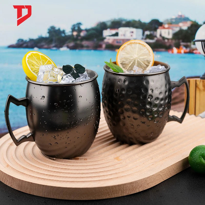 Black hammered copper insulated mugs with handles, filled with ice, lemon and lime slices, displayed on wooden board overlook