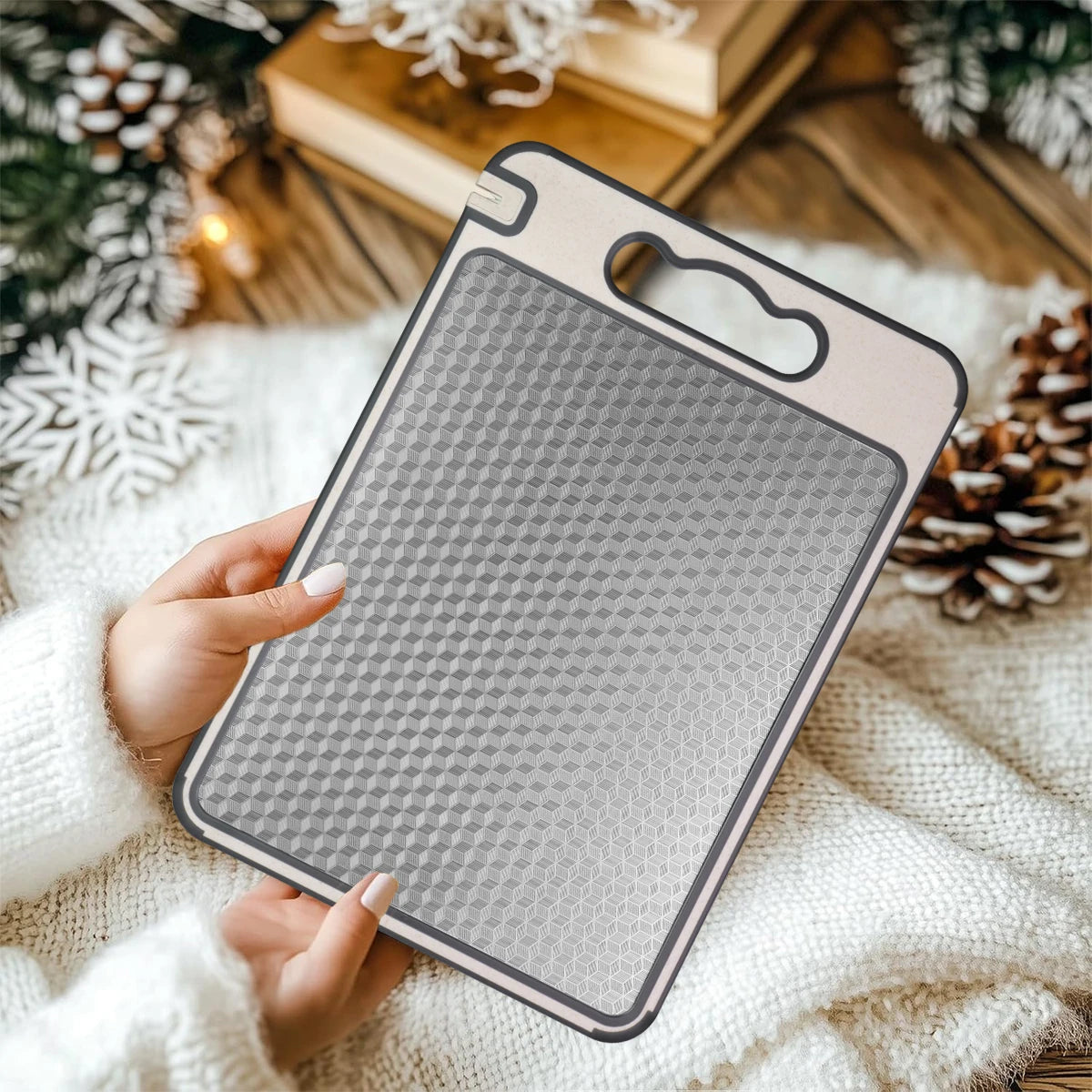 Stainless steel cutting board with honeycomb slip-resistant pattern, held in hands against festive holiday background with ev